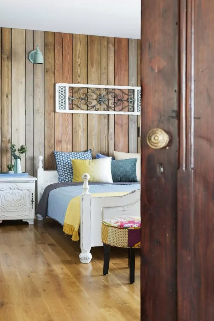 Kolorowe mieszkanie,mieszkanie boho,dekoracja nad łóżkiem panel drewniany,ściana obita drewnianymi dechami w kolorze drewna, niebieskie kinkiety vintage, rzeźbione fronty szafek nocnych w kolorze białym