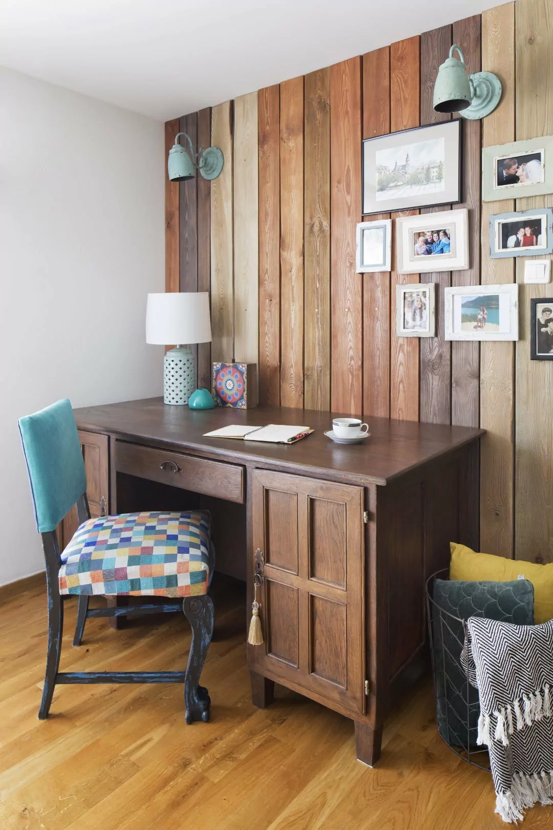 Kolorowe mieszkanie,mieszkanie boho,biurko drewniane, fotel niebieski kolorowe siedzisko, poduszki i koc w koszy metalowym, sciana obita drewnianymi dechami