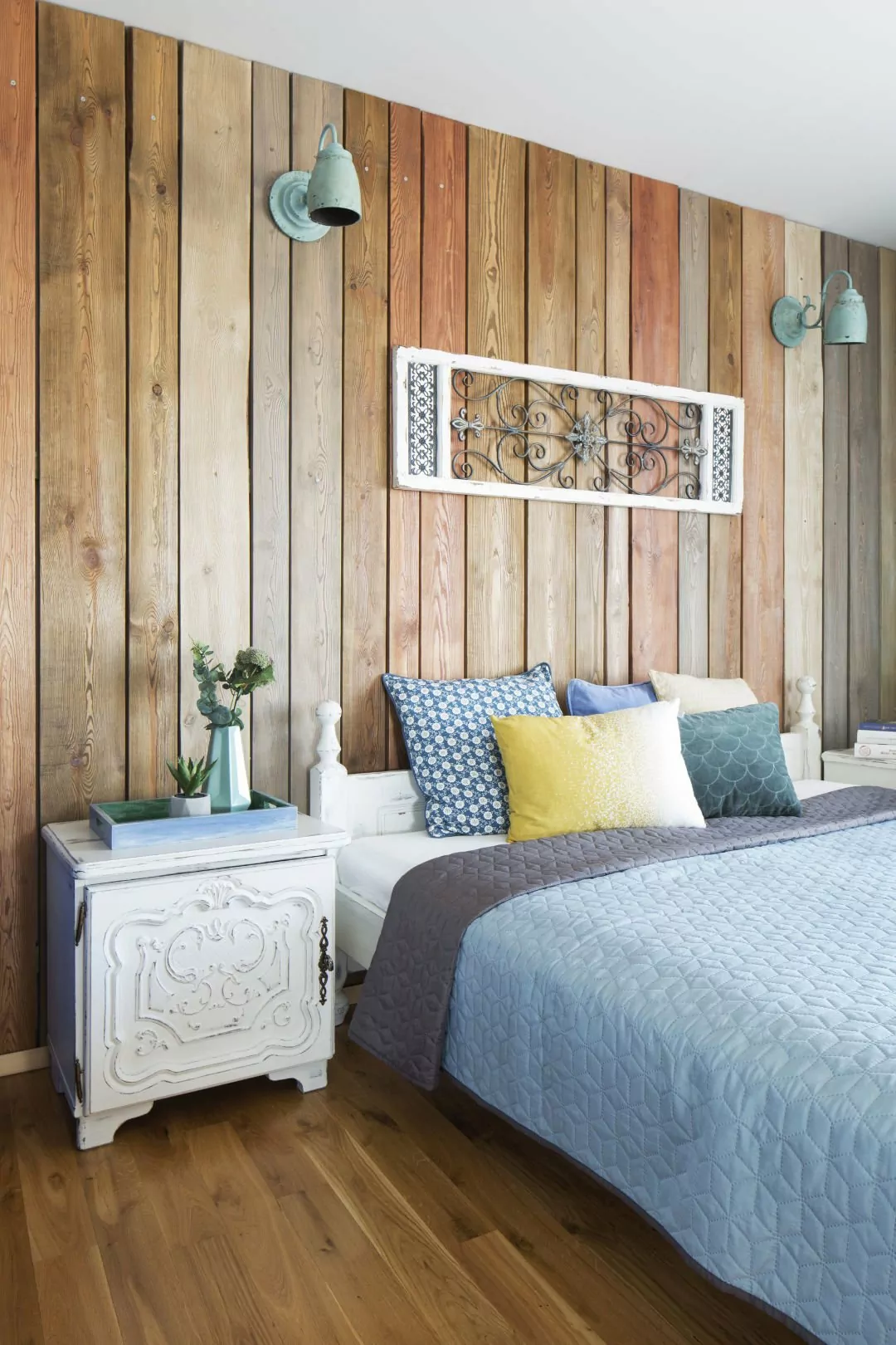 mieszkanie boho,dekoracja nad łóżkiem panel drewniany,ściana obita drewnianymi dechami w kolorze drewna, niebieskie kinkiety vintage, rzeźbione fronty szafek nocnych w kolorze białym
