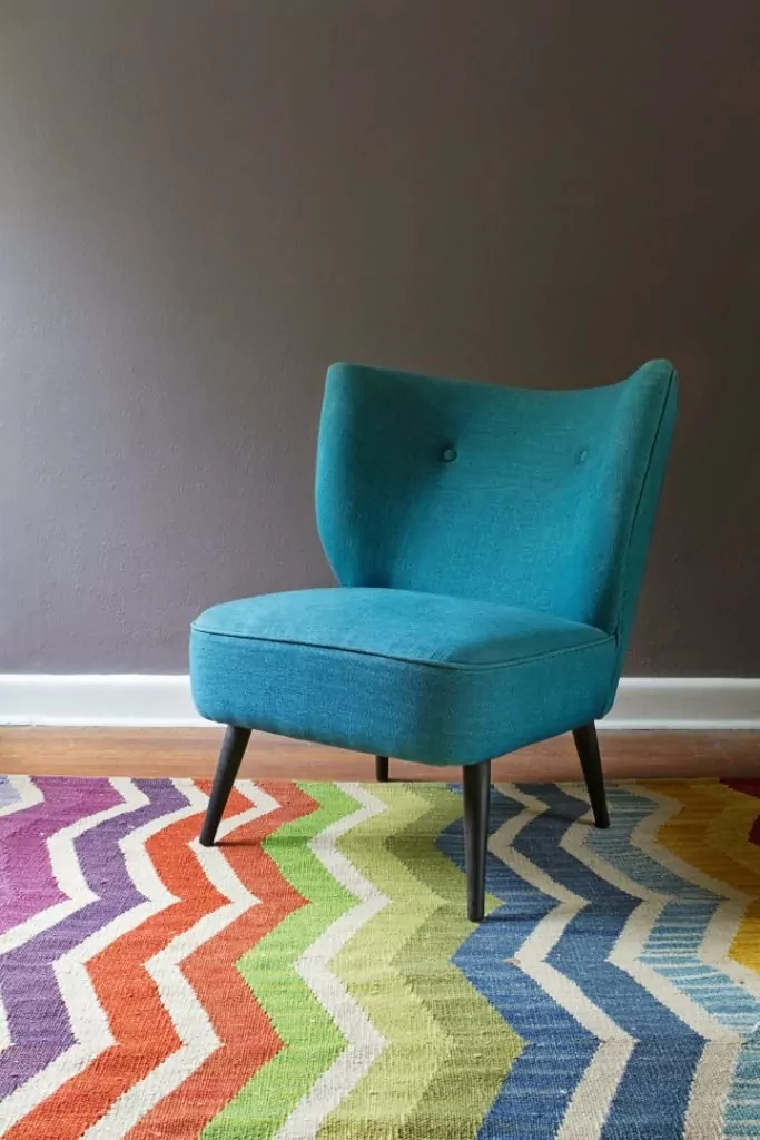 Kolor w salonie,Turkusowy fotel Chevron,kolorowy dywan, w tle ciemna ściana