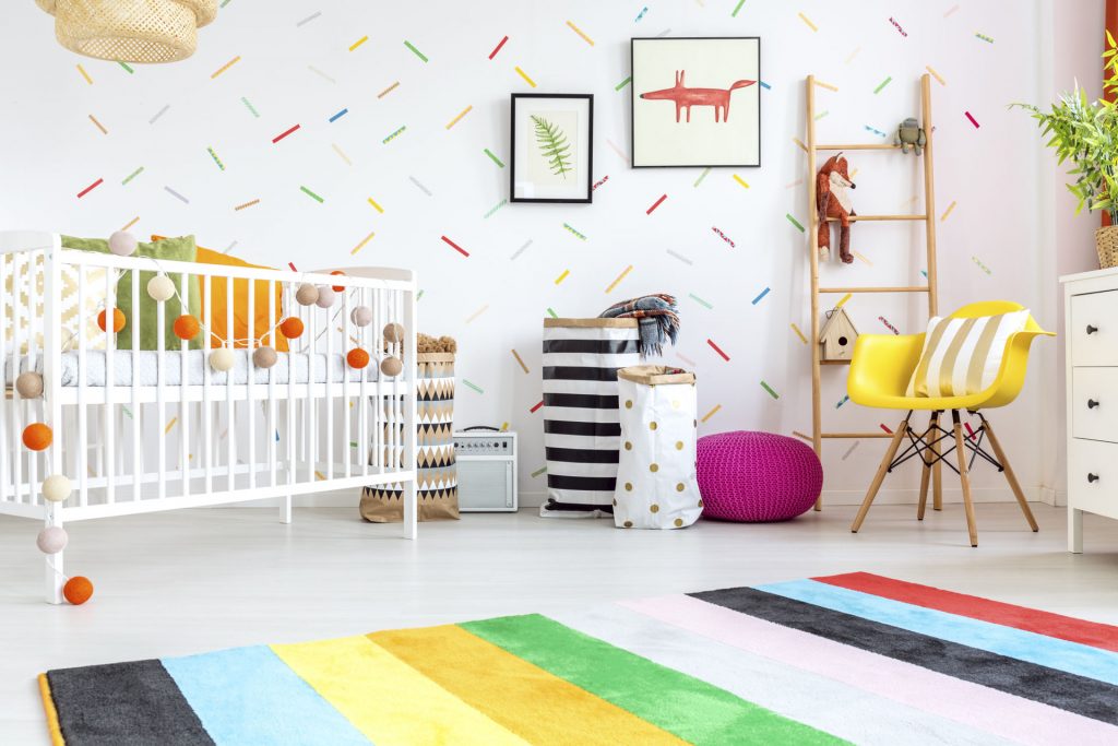 pokój dziecka- dekoracje, kolorowa tapeta wzór konfetti, żółty fotel, białe łóżeczko,różowa pufa