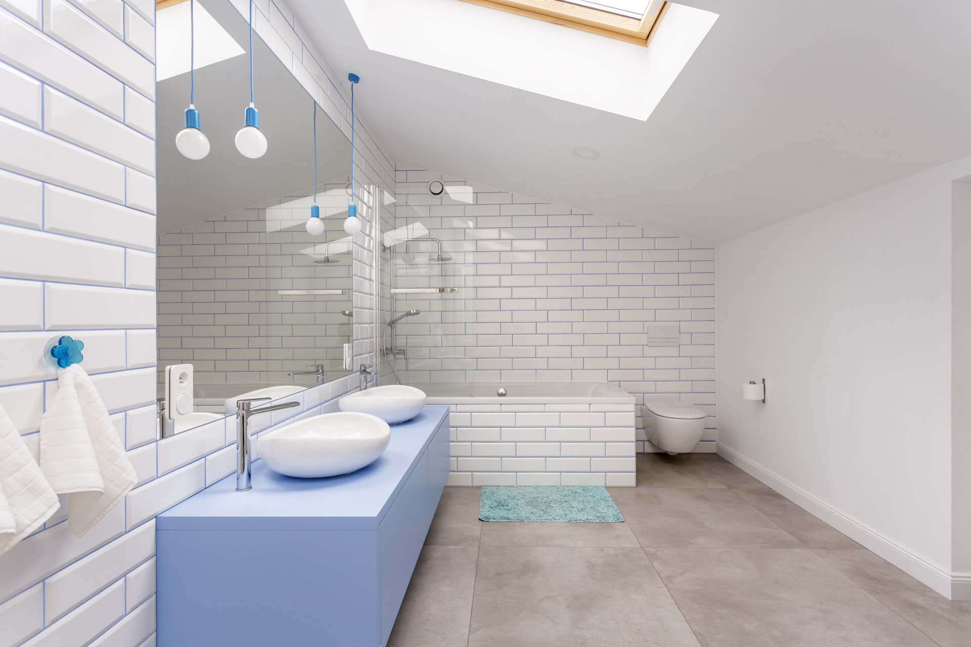 Niebieski w mieszkaniu, łazienka na poddaszu, niebieska szafka pod dwie umywalki, WC i wanną płytki białą cegła