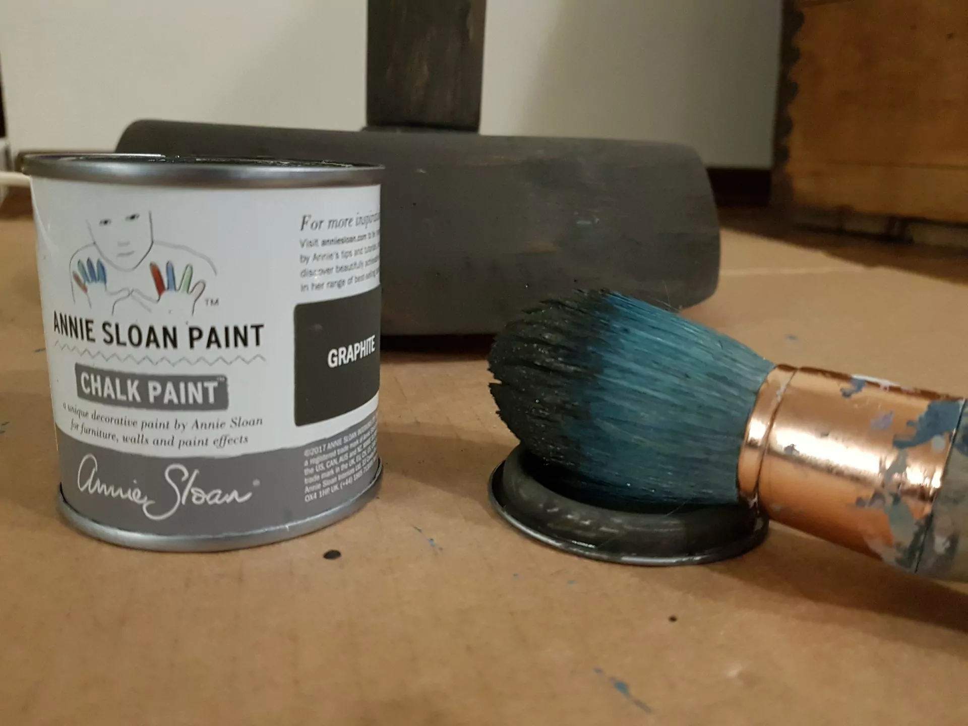 jak odnowić lampę, pędzel ubrudzony szarą farbą, puszka farby kredowej Annie Sloan kolor Graphite, w tle pomalowana na szaro podstawa lampy podłogowej