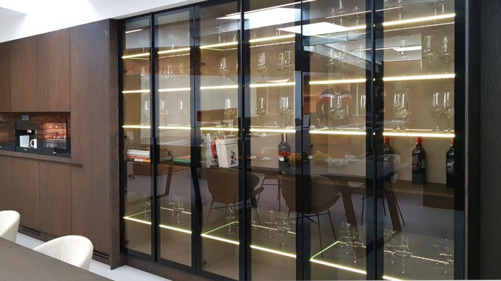 Ecomalta_witryna kuchenna_1200_machinasnu.pl Ecomalta, Studio Prostych Form, meble kuchenne z zabudowanym ekspresem do kawy, zabudowa kuchenna w ciemnym brązie, obok przeszklona witryna w czarnej ramie