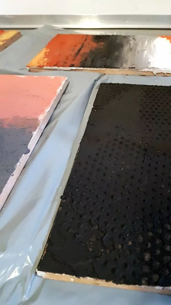 Ecomalta, co na podłogę, okładzina, panel z odpiśnientym wzorem w Ecomalcie, kolor czarny szary czerwony, panele leżą na podłodze pośród innych paneli