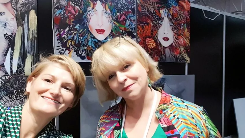Targi Gift&Deco, zdjęcie z targów, twarze dwóch kobiet robią selfie, uśmiechnięte kobiety ubrane w kolorowe bluzki, za nimi kolorowe obrazy