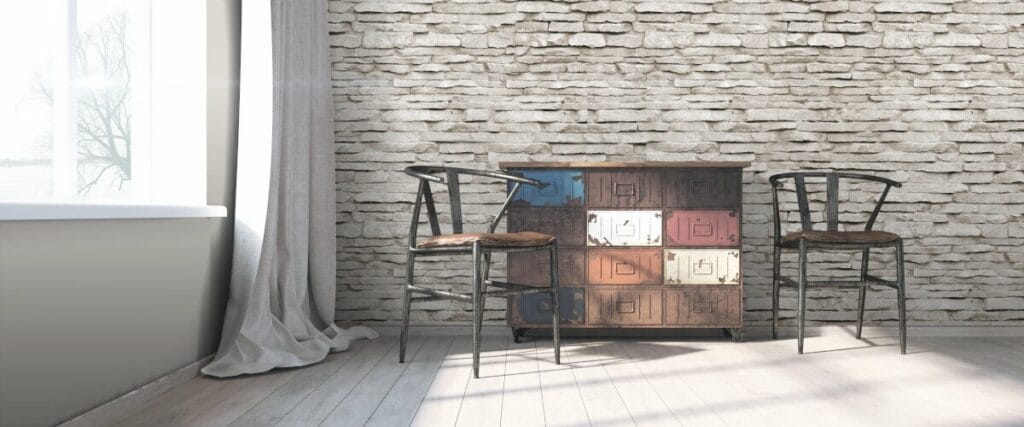 Nowoczesne wnętrze w stylu loft. Na tle ściany ze starej szarej cegły komoda z szufladami obok stoją dwa stare, drewniane krzesła