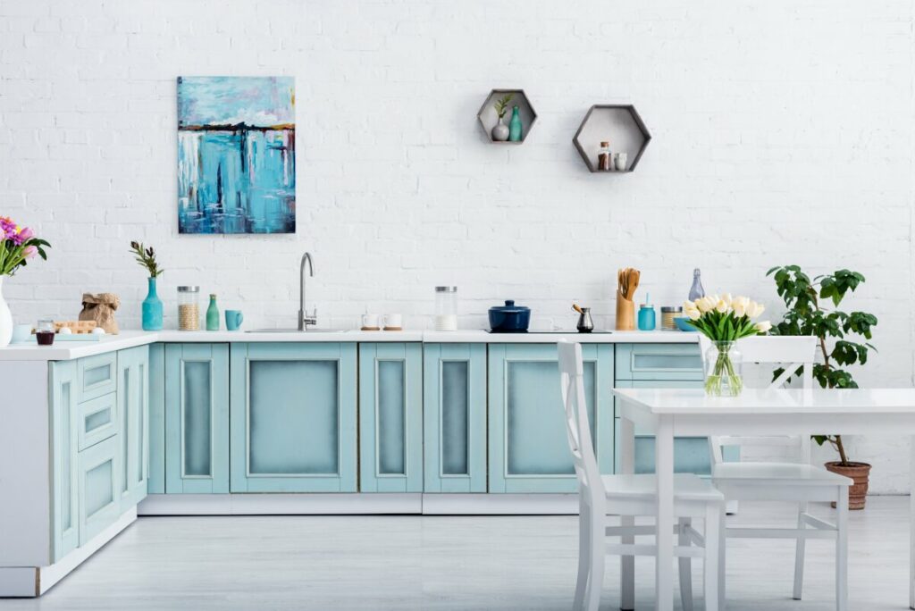Dekoracje do salonu, duża biała ściana ze starą białą cegłą, rząd szafek kuchennych w kolorze niebieskim, szafki kuchenne pomalowane farbą kredową, szafki kuchenne pomalowane i cieniowane, kuchnia z białym blatem