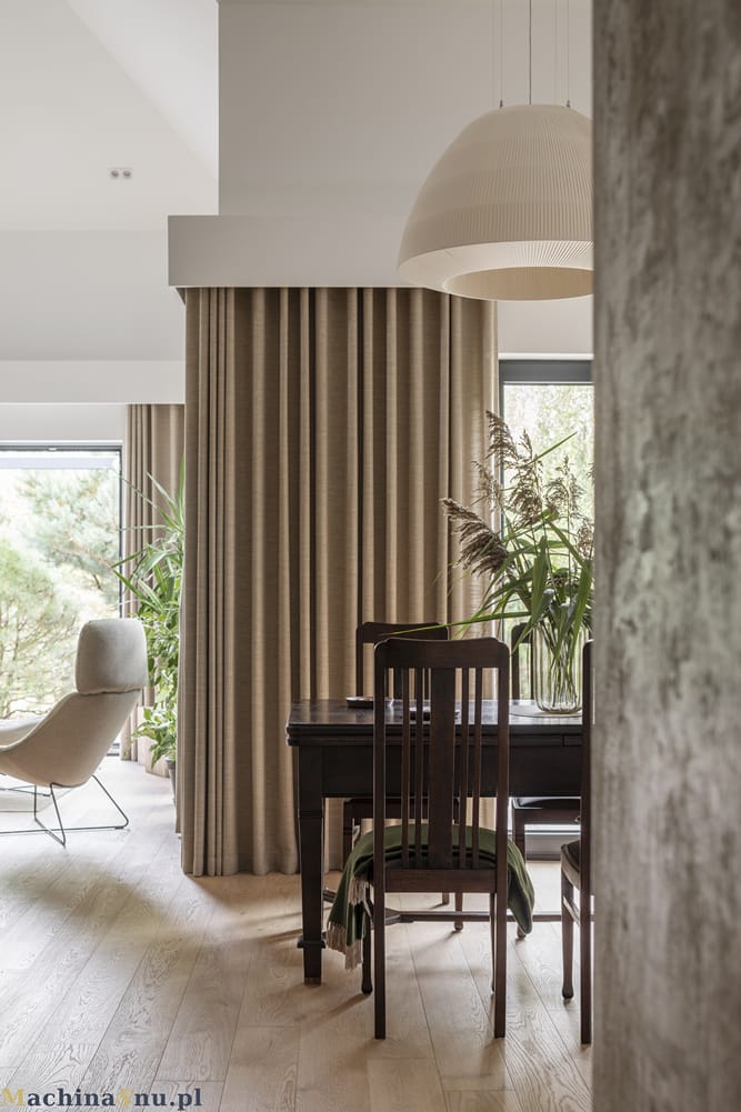 Antyczny stół jadalniany stojący przy dużych, szklanych drzwiach, przez które widać zielony ogród.