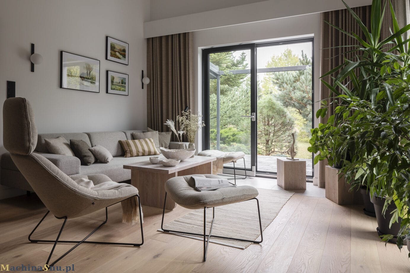 Jasny salon z dużą, beżową sofą i nowoczesnymi fotelami. Przez duże, szklane drzwi widać sosnowy ogród.
