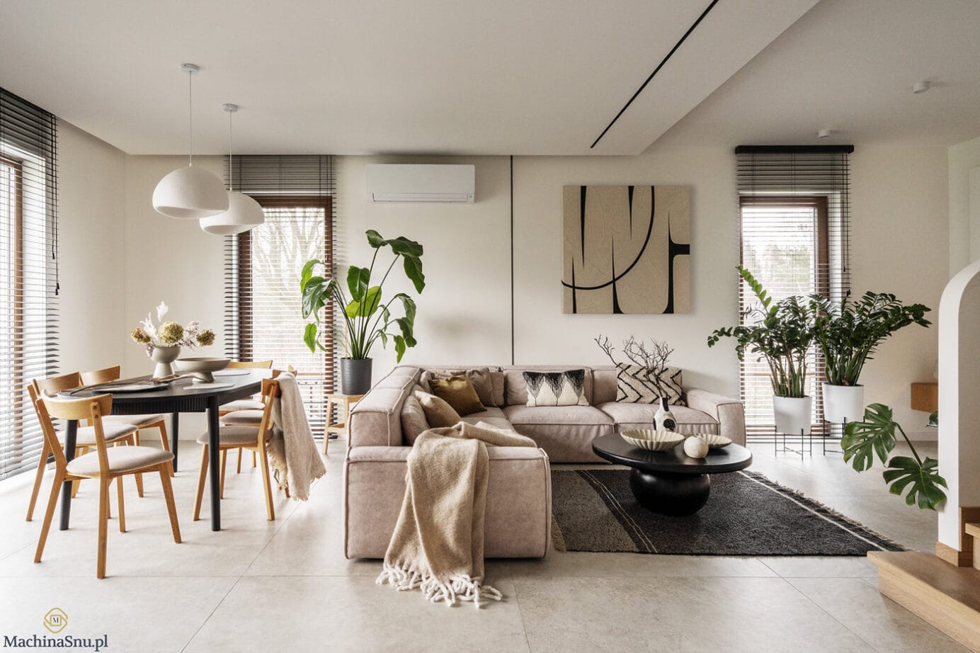 Przestronny salon połączony z jadalnią. Beżowa sofa narożna, czarny stół, drewniane krzesła i duże okna z żaluzjami.