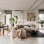 Przestronny salon połączony z jadalnią. Beżowa sofa narożna, czarny stół, drewniane krzesła i duże okna z żaluzjami.