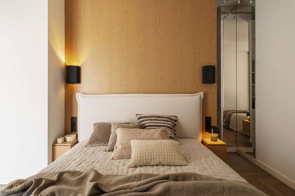 Widok na ł&oacute;żko w sypialni master. Fornirowana zabudowa ścienna, lustrzane drzwi do garderoby i dębowa podłoga w jodełkę.
